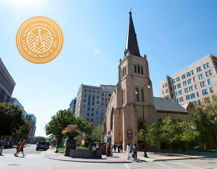 A stone church with a tall steeple sits at a busy city intersection, surrounded by trees and modern buildings. The logo for Grace Episcopal Church, reading “Enduring Sanctuary,” is overlaid in the sky.